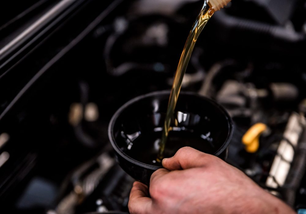 Close up of male hands adding oil with a funnel after a do-it-yourself oil change. Selective focus